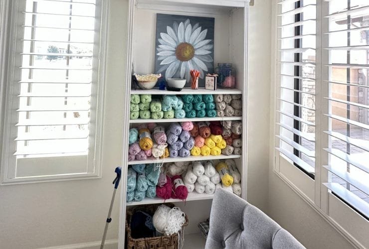 A neatly organized shelf full of yarn and a cozy chair in a room.