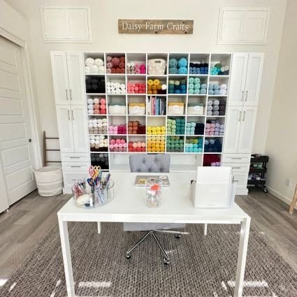 A professional organizer's dream craft room, complete with a white desk and an abundance of yarn.