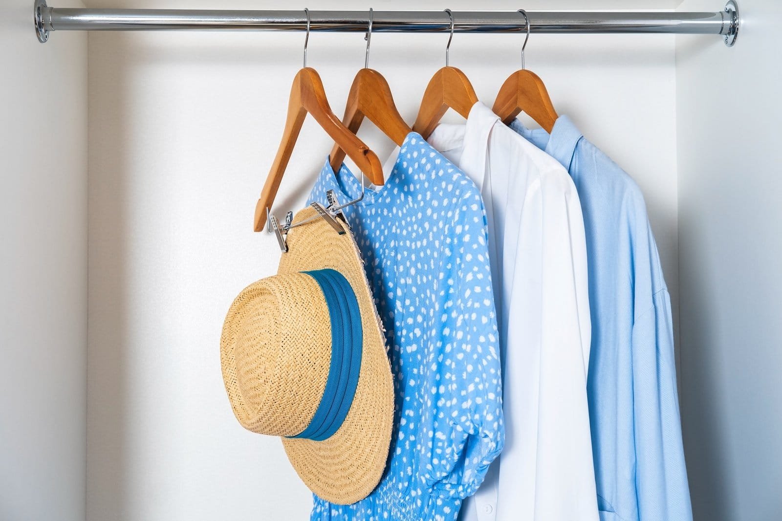Professional organizer arranges clothes and a hat on a hanger in a closet.